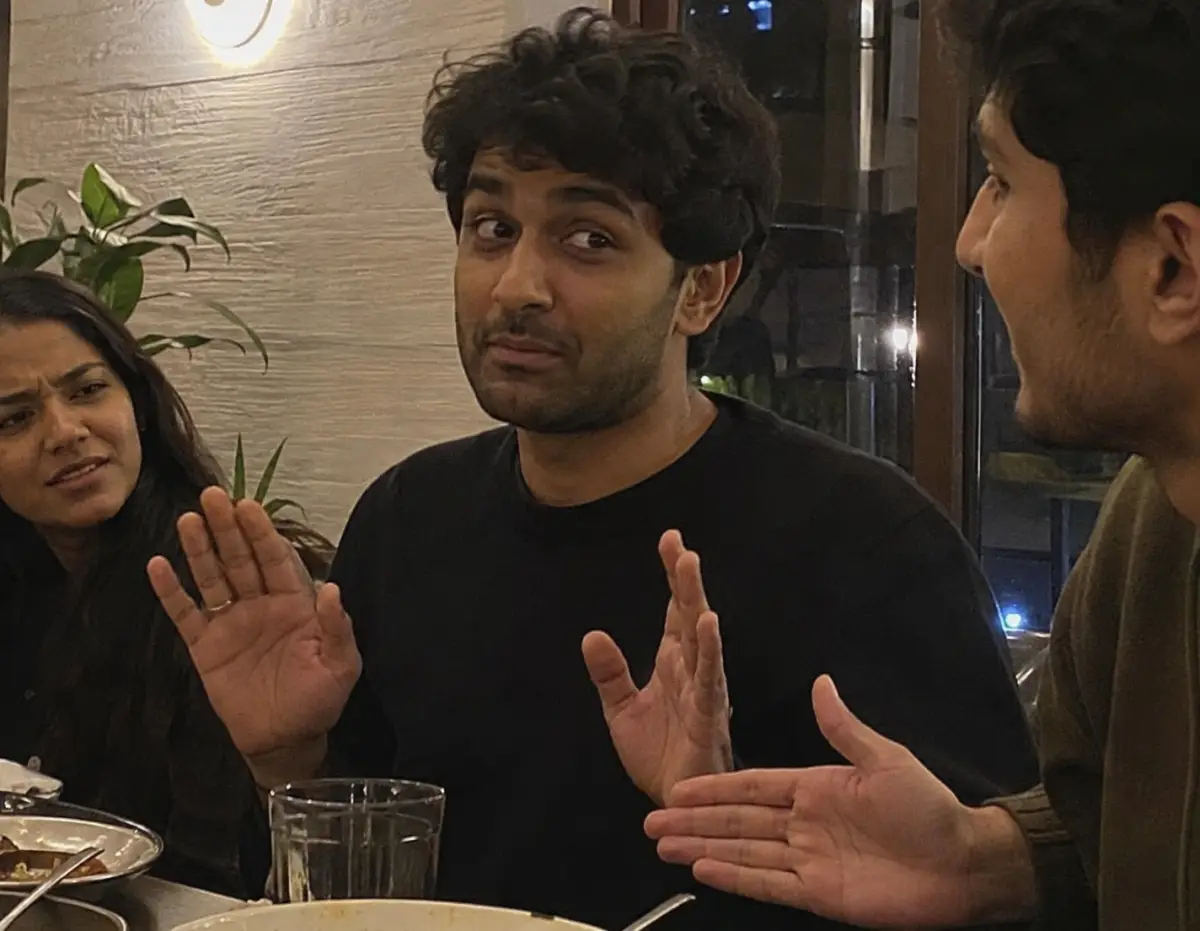 Someone mid-apology gesture at a dinner table while friends look slightly awkward