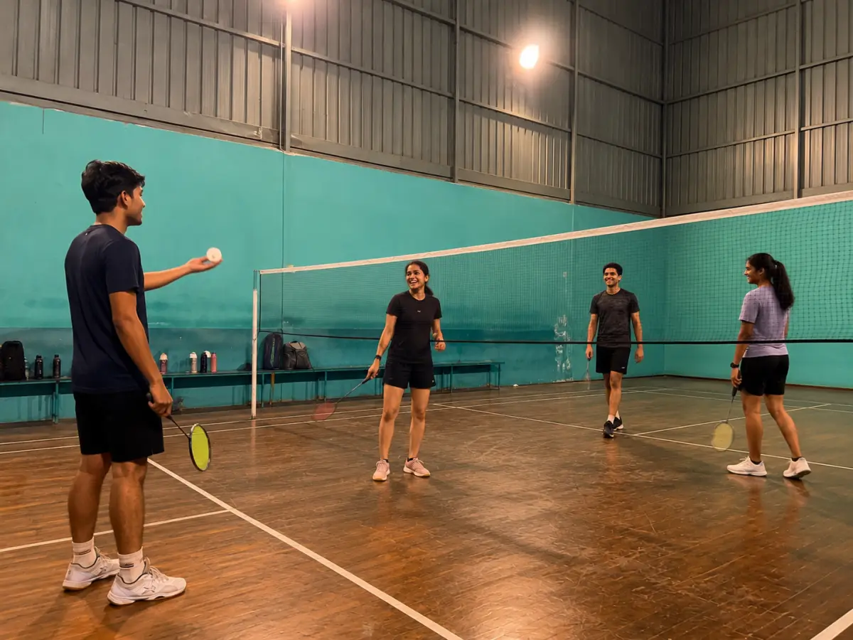 Mixed-level doubles on an indoor court, one player feeding shuttles while others rotate in